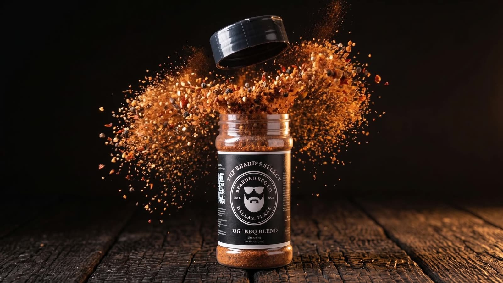 The Beard's Select OG BBQ Blend seasoning jar on a dark charred wood surface.